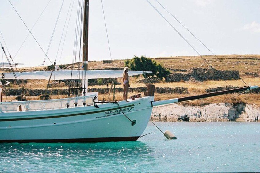 A sailboat named 'Dolphins of the Isles' anchored near rocky shore with a person standing on the deck. 2