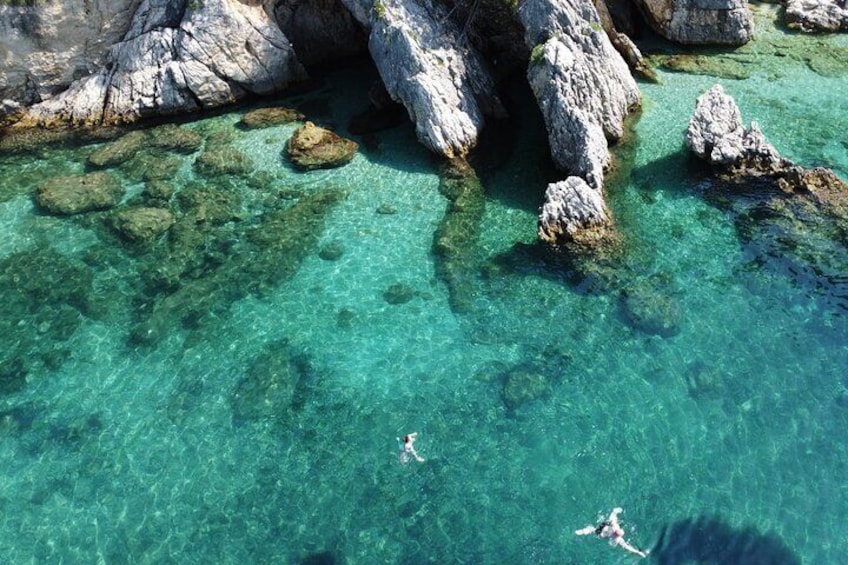 A clear turquoise sea with two people swimming near rocky formations. 3