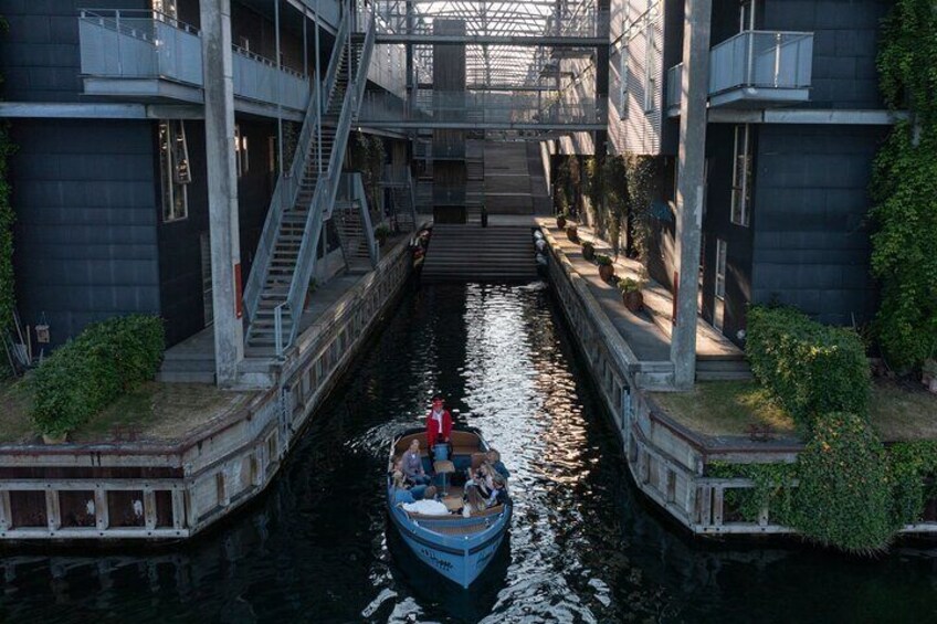 En smal kanal med en båd fyldt med passagerer, med bygninger med trapper og gelændere langs siderne. 5