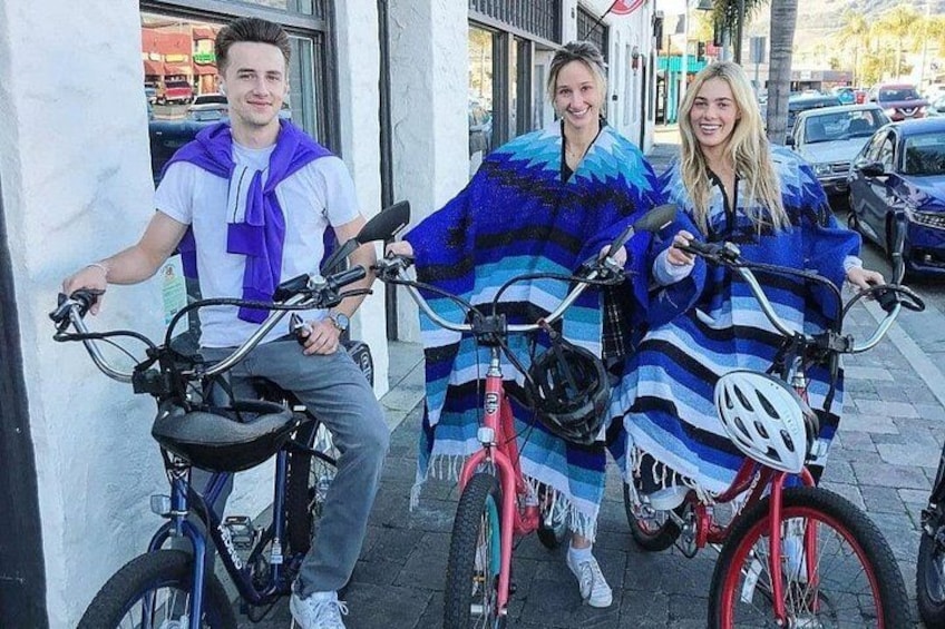 Three people on bicycles, one with a purple scarf, another with a blue scarf, and the third with a white helmet. 1