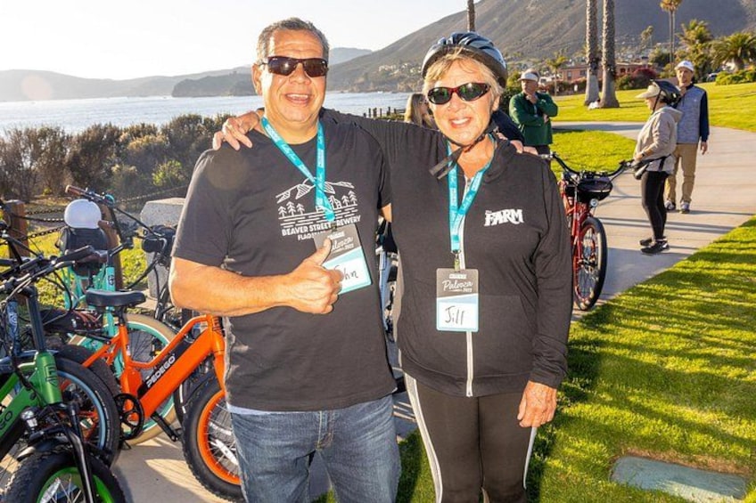 Two people standing by bicycles, with a scenic view of a body of water and hills in the background. 3