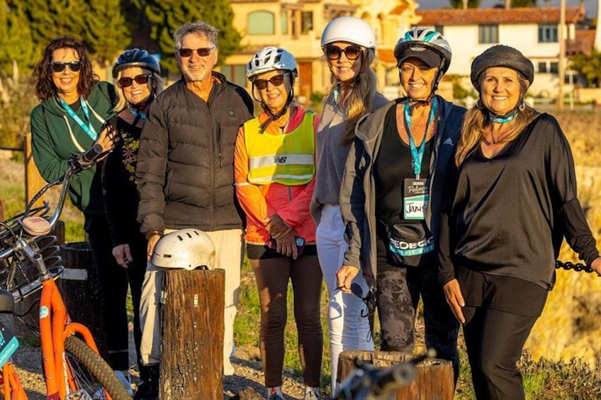A group of people with bicycles and helmets, standing outdoors with a wooden post and a building in the background. 4
