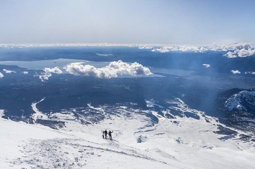 A snowy mountain landscape with two hikers, a vast body of water, and distant clouds. 5