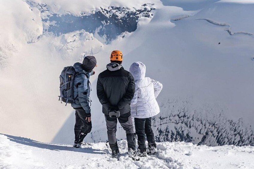 Three people standing on a snowy mountain peak, looking at the landscape. 2