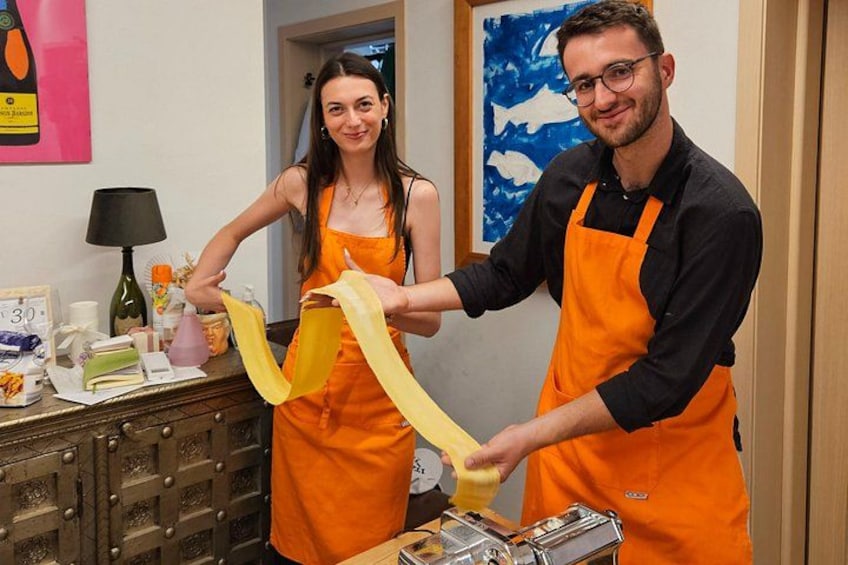 Due persone con grembiuli arancioni che preparano cibo, con utensili da cucina e una lampada sullo sfondo. 3