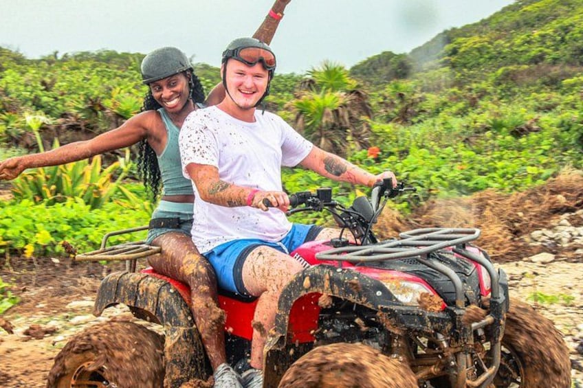 Two people on a muddy ATV in a tropical setting with dense vegetation. 5