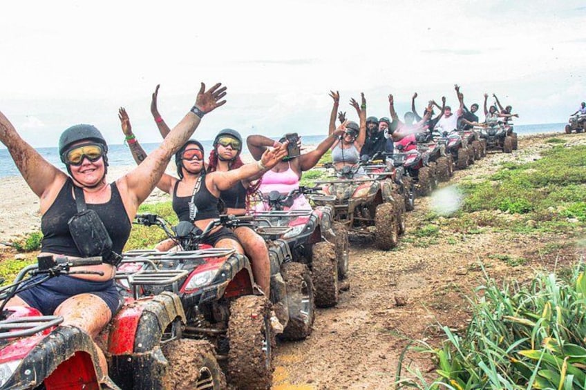 A group of people on ATVs on a muddy path near a beach. 4
