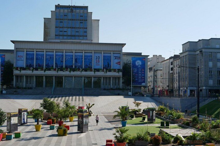 A plaza with a modern building, potted plants, and a clear sky. 3