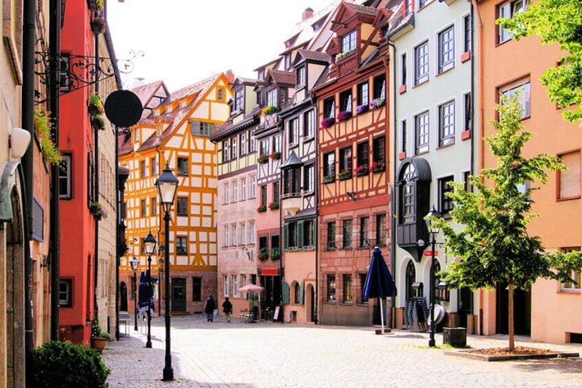 A cobblestone street lined with colorful half-timbered buildings, a lamppost, and a tree. 2