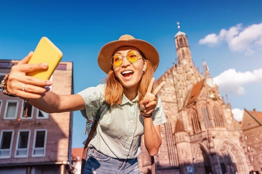 A person taking a selfie with a yellow phone, wearing a straw hat and a striped shirt, with a historic building in the background. 5
