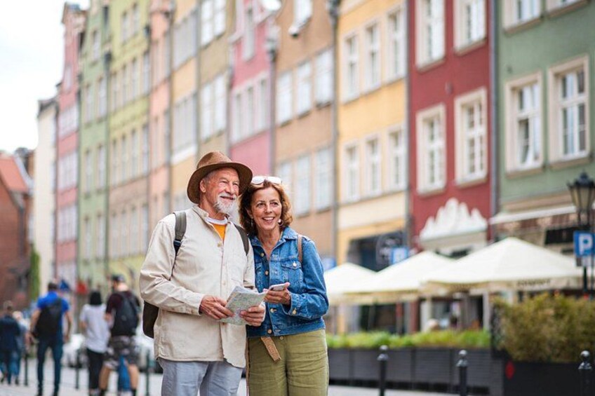 A couple holding a map, standing in front of colorful buildings with a street and umbrellas in the background. 4
