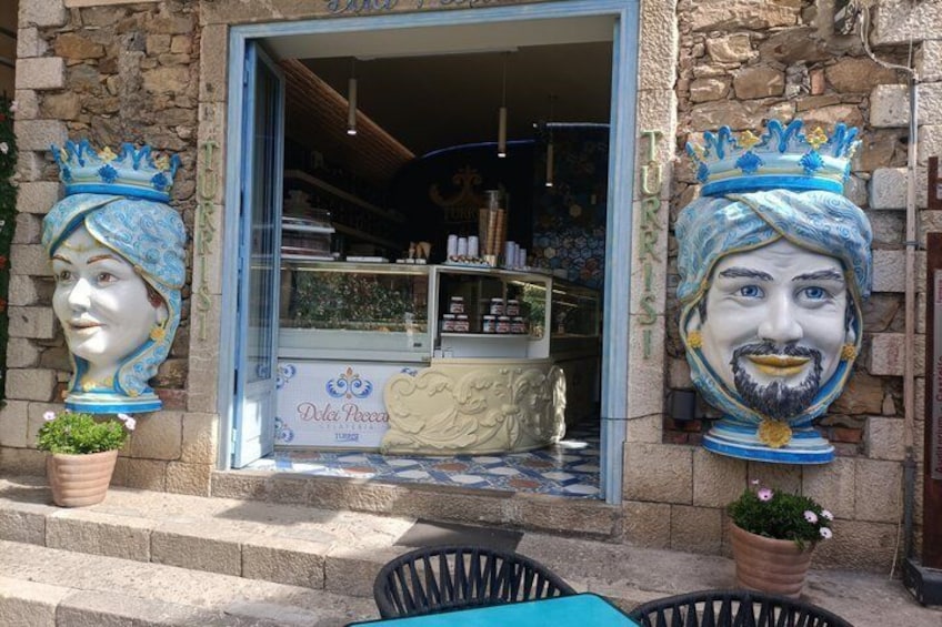 Une devanture de magasin avec une enseigne bleue et blanche, deux sculptures de tête décoratives et une plante en pot. 4