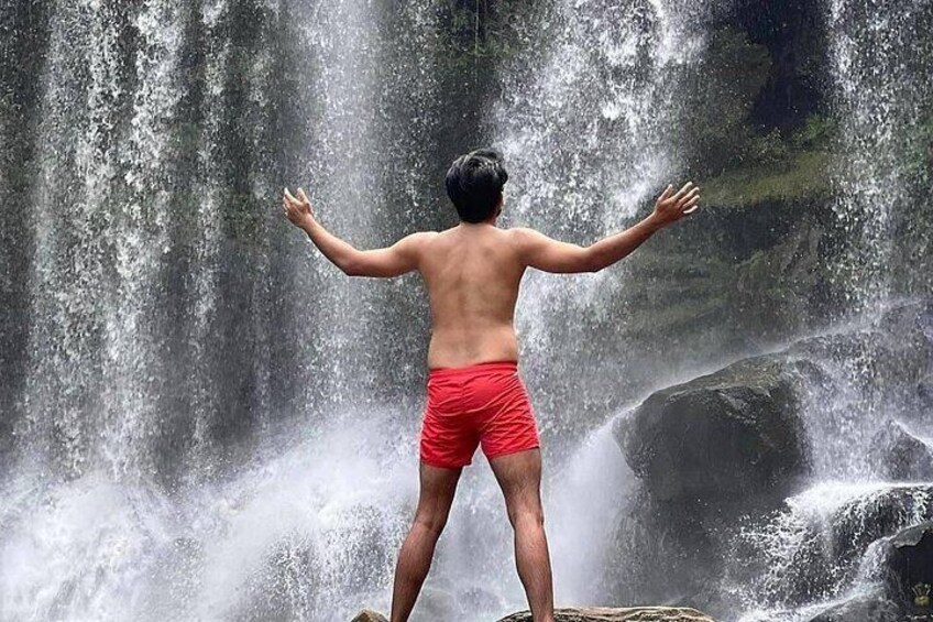 A person standing on a rock with arms outstretched in front of a waterfall. 5