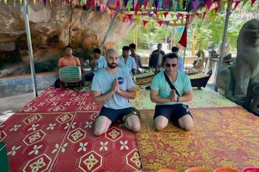 Two people sitting on patterned mats in a cave-like setting with a stone statue in the background. 3