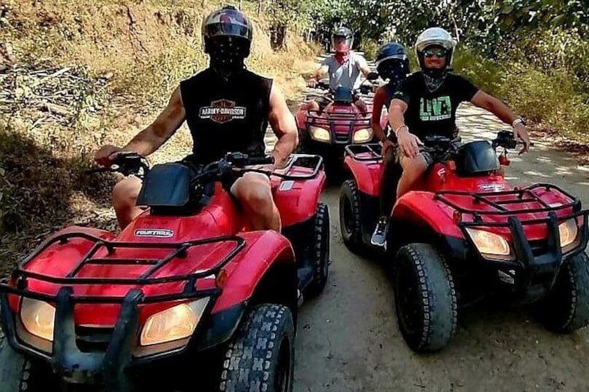 Vier personen rijden op rode quadbikes over een zandweg. 1