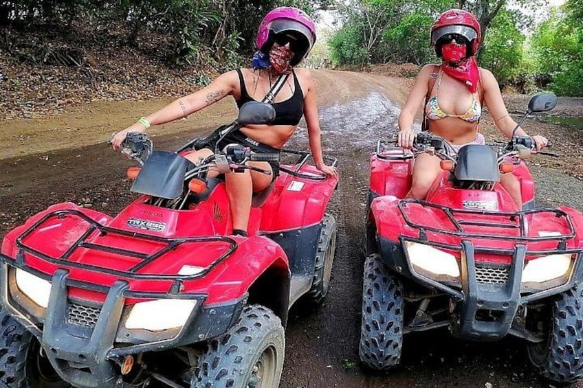 Twee personen op rode terreinwagens op een zandpad, met begroeiing op de achtergrond. 5