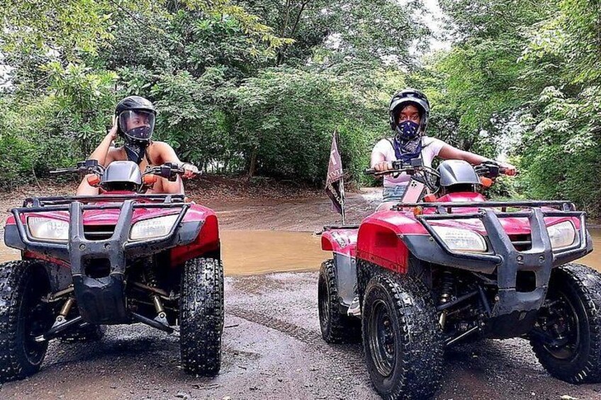 Twee personen op rode quadbikes op een modderige pad met bomen op de achtergrond. 4