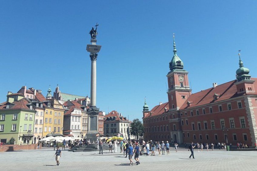 A public square with a tall monument, historic buildings, and a clear blue sky. 1