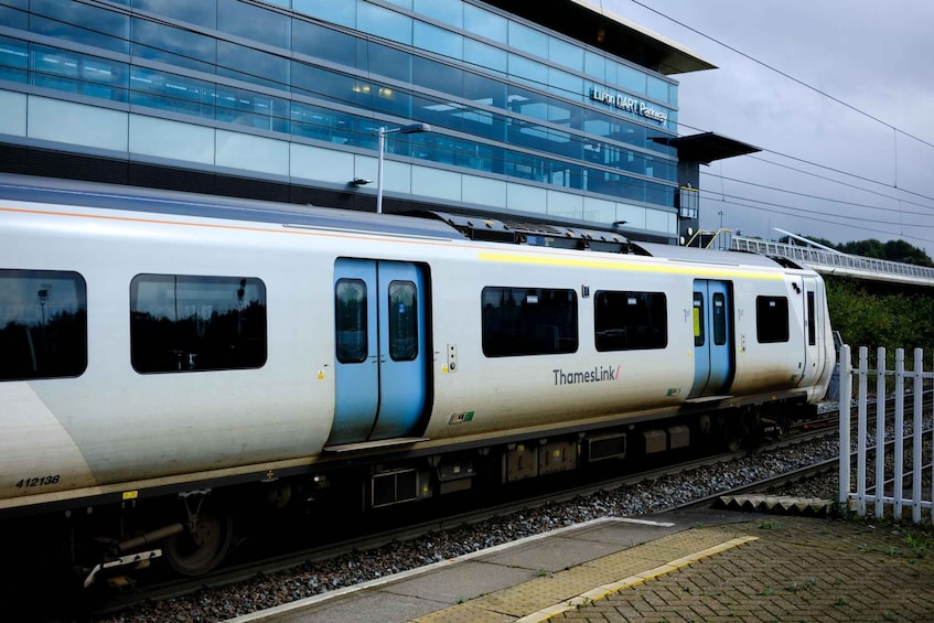 A white and blue ThamesLink train at a station with a modern glass building in the background. 5