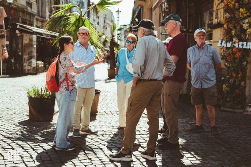 Een groep mensen staat op een geplaveid straatje en voert een gesprek. 1