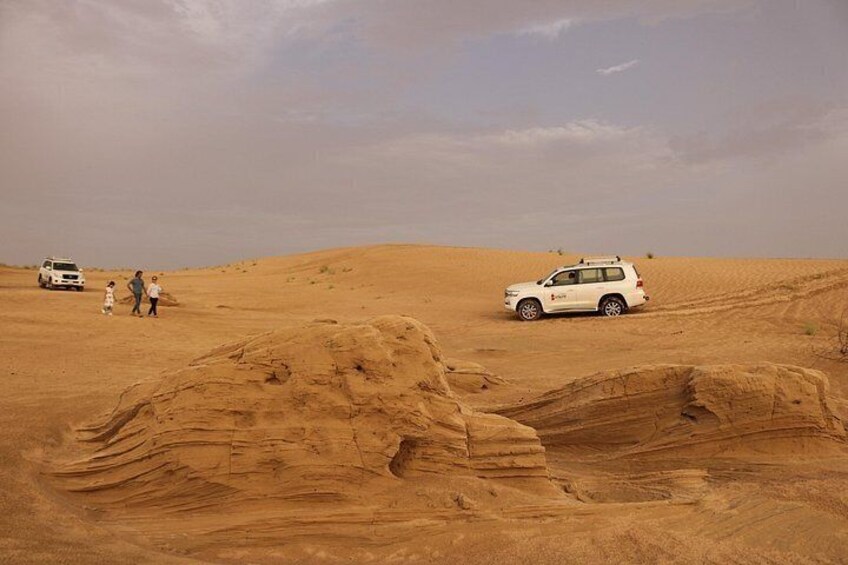 A desert landscape with sand dunes and a white SUV parked on the sand. 5