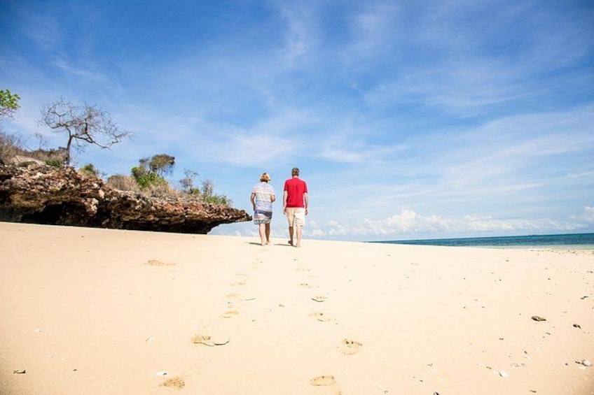 A beach with footprints leading towards the ocean, a rocky outcrop, and a clear sky. 4