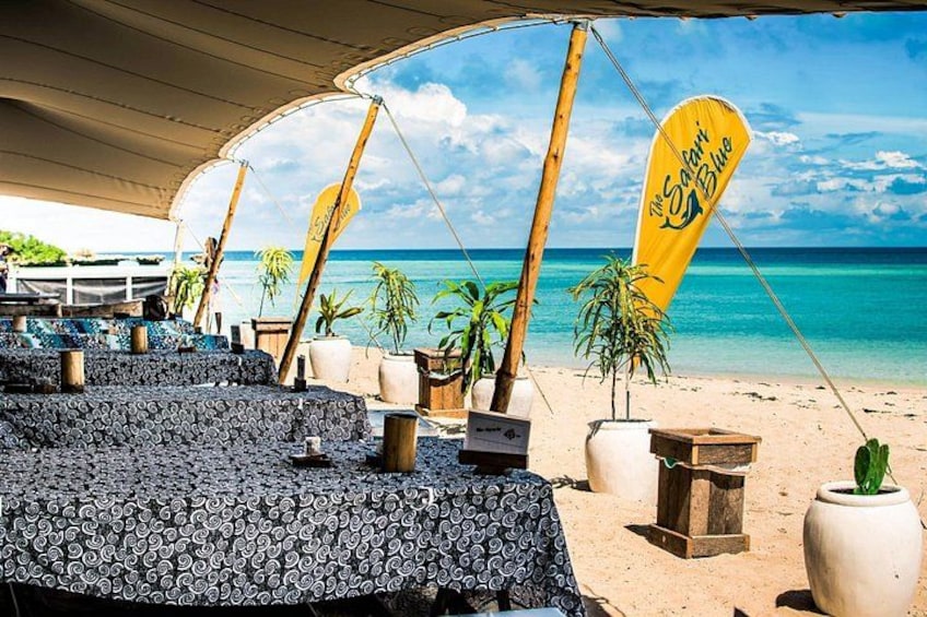 A beachside restaurant with outdoor seating, palm trees, and a clear view of the ocean. 5