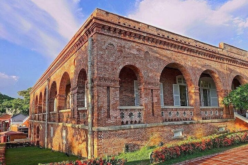 A brick building with arched windows and a garden in front. 5