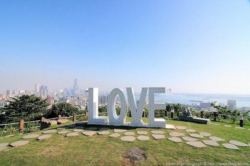 Large metallic letters spelling 'LOVE' on a grassy hill with a cityscape in the background. 3