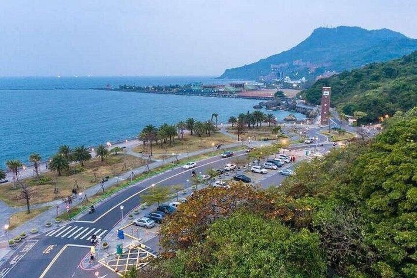 A coastal road with vehicles, a pedestrian crossing, and a hill with a tower. 4