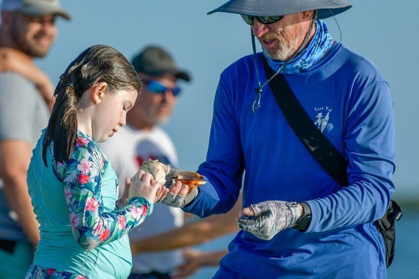 A person in a blue shirt and hat handing something to a child in a floral shirt. 4