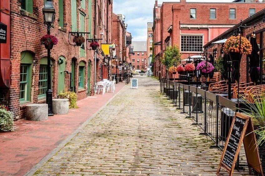 A cobblestone street lined with brick buildings, outdoor seating, and hanging flower baskets. 5