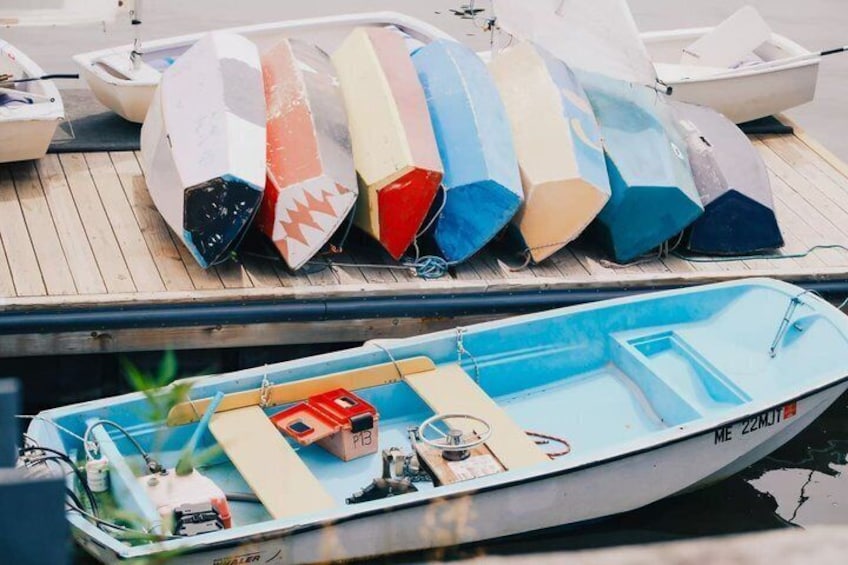 A row of colorful surfboards on a dock, a small boat with a blue interior, and a red box on the boat's deck. 3