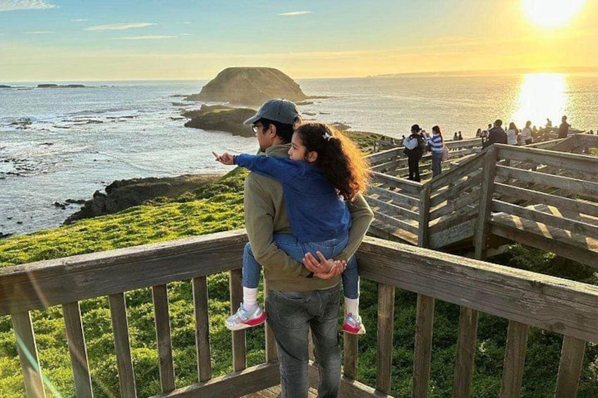 A couple on a wooden observation deck overlooking a coastal landscape with a sunset. 2
