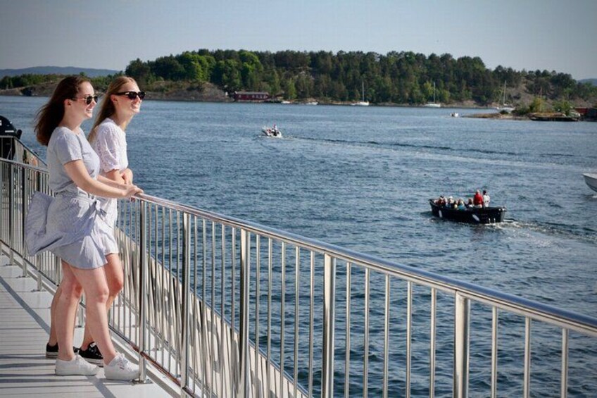Dos personas en un muelle con vista a un lago, barcos y una orilla arbolada. 4