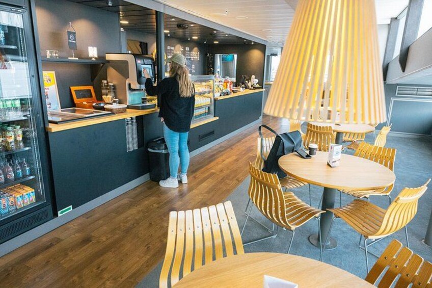 Interior de una cafetería moderna con mesas y sillas de madera, una barra con máquina de café y una persona haciendo un pedido. 2