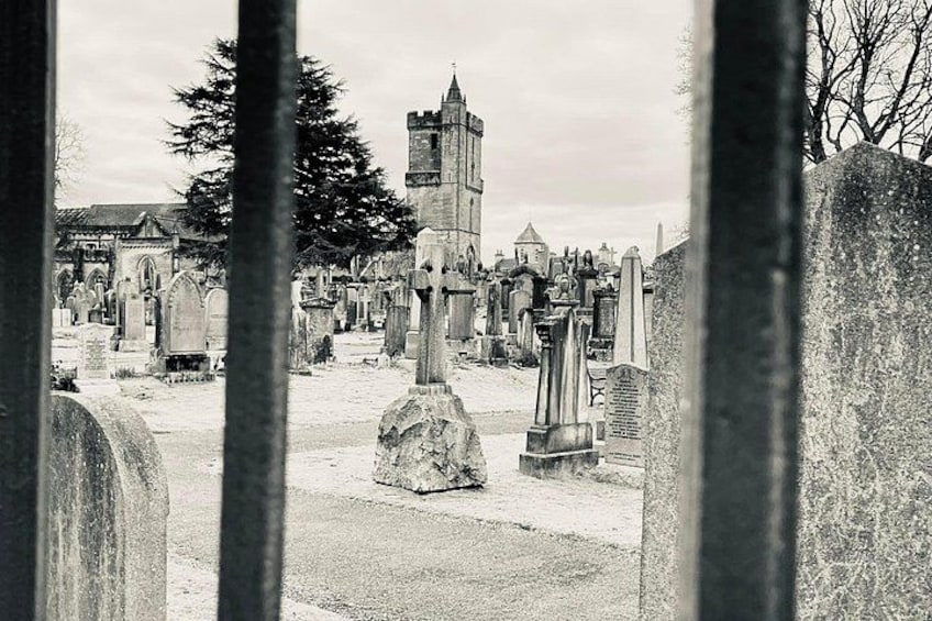 Un cimetière avec des pierres tombales, un grand arbre et le clocher d’une église. 4