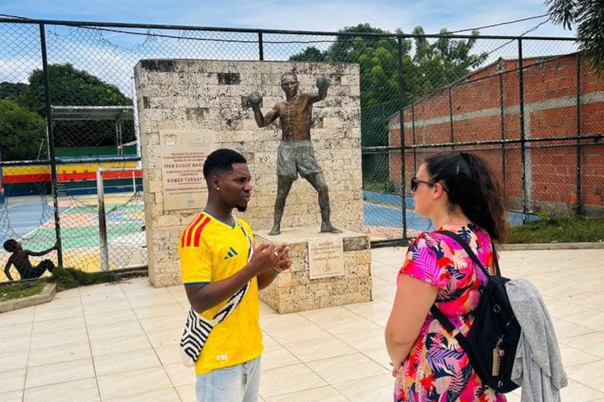 A man in a yellow jersey and a woman in a colorful dress standing in front of a statue. 4