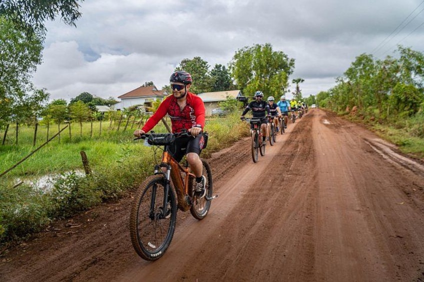 En gruppe cyklister på en grusvej med grønt på begge sider. 2