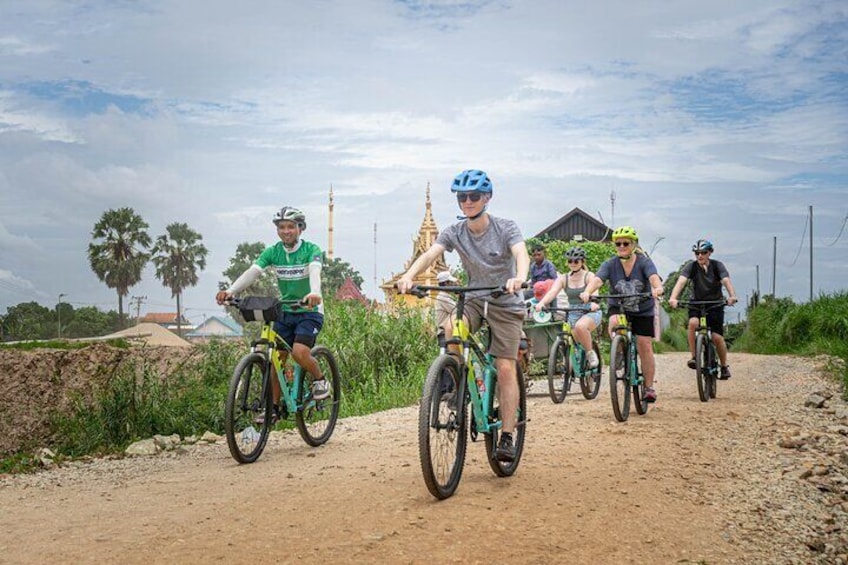 Un grupo de ciclistas en un sendero de tierra con un templo al fondo. 1