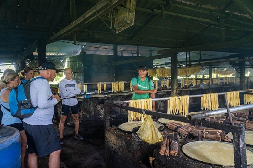 Un grupo de personas observando un proceso de cocina en una rústica cocina con fideos colgando y utensilios de cocina. 4