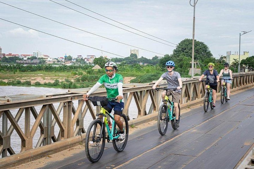 Tres ciclistas sobre un puente, con un paisaje urbano al fondo. 5