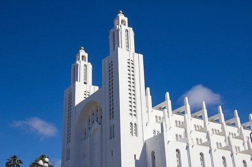 Un edificio blanco con dos torres y una amplia entrada en arco bajo un cielo azul despejado. 3
