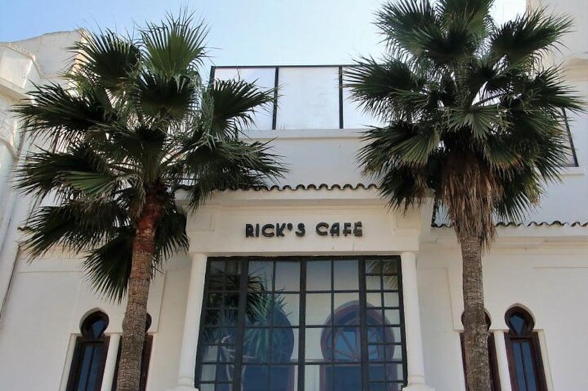 Een gebouw met een bord waarop 'Rick's Cafe' staat, en palmbomen ervoor. 2
