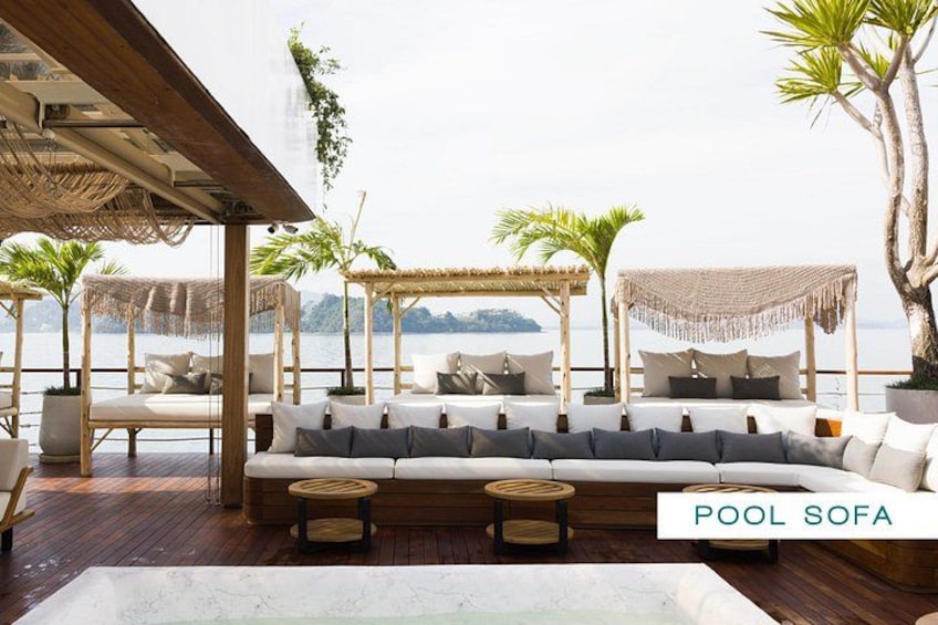 A poolside lounge area with a large sofa, lounge chairs, and a pergola with a canopy. 2