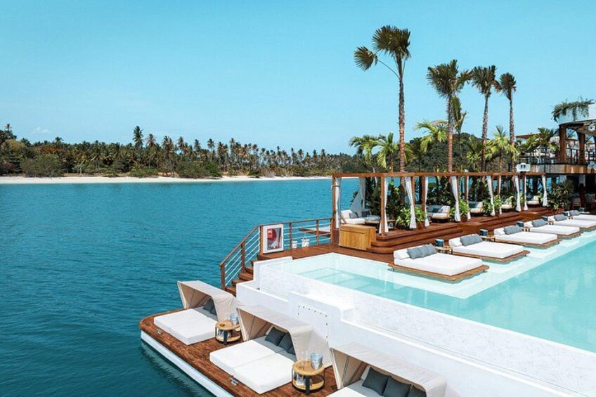 A floating pool with lounge chairs, palm trees, and a beach in the background. 2