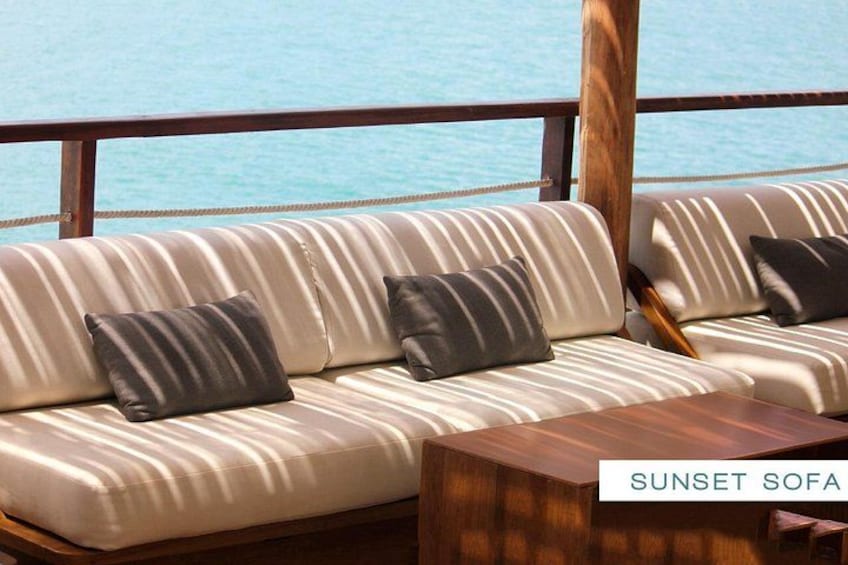 A sunset sofa with striped cushions, a wooden table, and a view of the ocean. 3