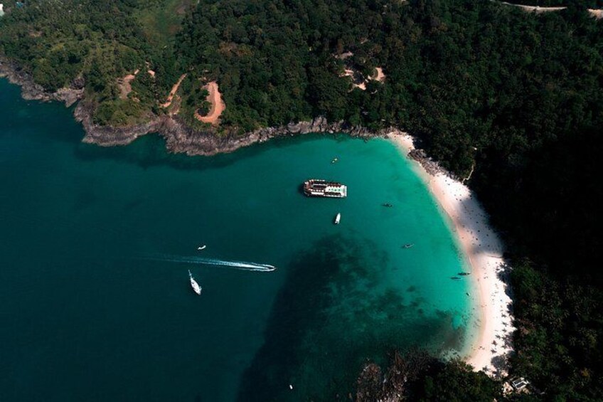 An aerial view of a coastal area with a sandy beach, clear turquoise waters, and a ship docked near the shore. 2