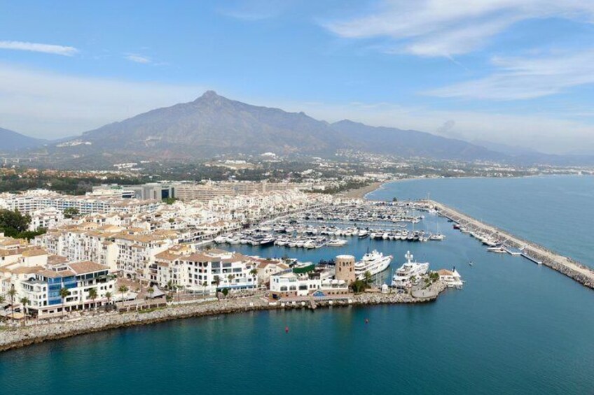 Un pueblo costero con un puerto deportivo, edificios y una montaña al fondo. 5