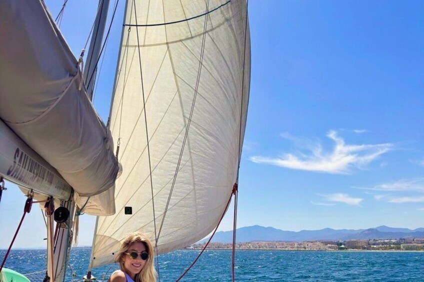 Un velero con una persona en la cubierta, un cielo azul despejado y una costa distante con montañas. 4